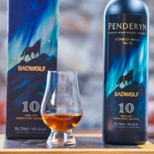 Two bottles of Penderyn Badwolf whisky with a glass of whisky on a wooden surface.