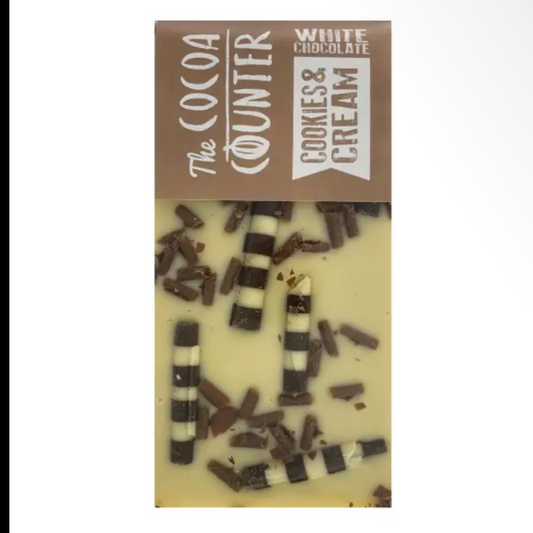 A vertical chocolate bar package labeled 'The Cocoa Counter' with 'White Chocolate Cookies & Cream' written on it. The bar itself is pale cream with dark chocolate cookie pieces embedded vertically and scattered throughout.